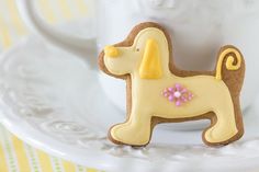 a cookie shaped like a dog sitting on top of a white plate next to a cup