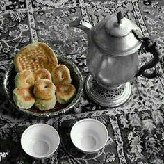 there is a silver tea pot and two cups on the table with pastries in front of it