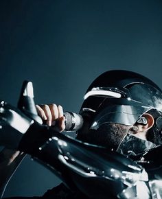 a man wearing a helmet and holding a microphone up to his face while standing in front of a dark background