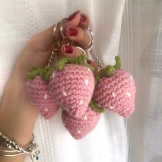 a hand holding two crocheted strawberries on a chain with green leaves and white polka dots