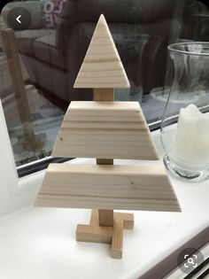 a wooden christmas tree sitting on top of a window sill next to a candle