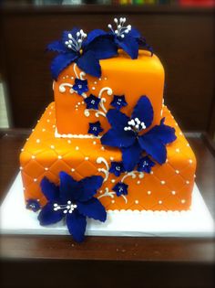 a three tiered orange cake with blue flowers on the top and bottom, sitting on a table