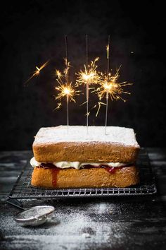 a cake with sparklers on it sitting on top of a cooling rack next to a spoon