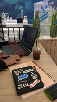 two people sitting at a table with laptops and notebooks in front of them