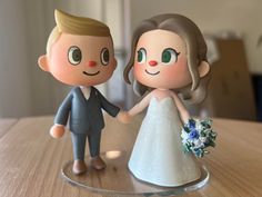 a bride and groom figurine holding hands on top of a wooden table next to each other