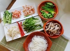 four bowls filled with food on top of a bamboo mat next to a bowl of noodles