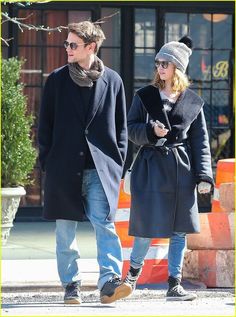 the man and woman are walking together down the street wearing winter clothes, hats and scarves