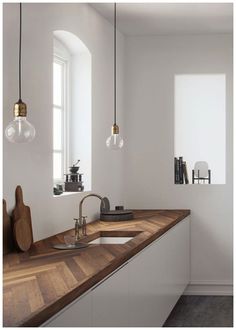 a kitchen with white walls and wooden counter tops, two hanging lights above the sink