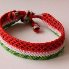 a red, white and green crochet bracelet on a white surface with a knot at the end