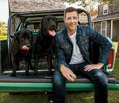 a man sitting in the back of a pick up truck with two dogs