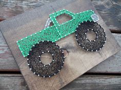 a green and black truck made out of string art on wood planks with white beads