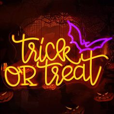 a neon sign that says trick or treat with bats and pumpkins in the background