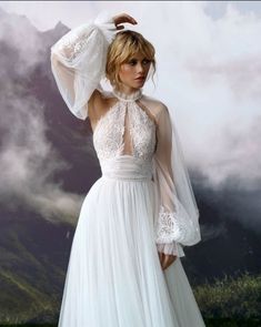 a woman in a white dress with a veil on her head and clouds behind her