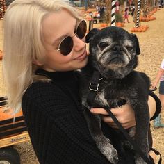 a woman is holding a small dog in her arms at an amusement park with pumpkins on the ground