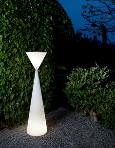 a white lamp sitting on top of a gravel ground next to trees and bushes at night