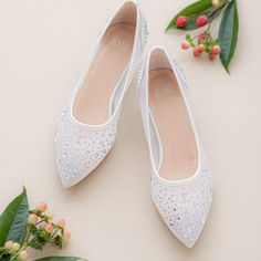 two pairs of white shoes sitting on top of a table next to flowers and leaves