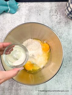 two eggs are being mixed in a bowl with flour and water on the side, while someone is holding their hand over the bowl