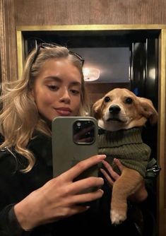 a woman taking a selfie with her dog wearing a sweater and holding a cell phone