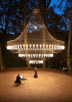 two people sitting on chairs under a chandelier in the middle of a park