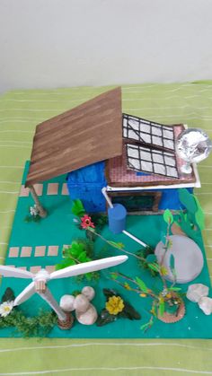 a small model house on top of a green mat with flowers and plants around it