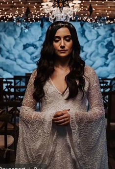 a woman wearing a white dress standing in front of a chandelier with lights