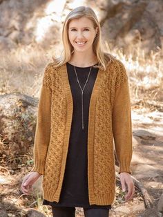 a woman standing in the woods wearing a brown cardigan sweater and black leggings