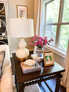 a table with flowers and pictures on it in front of a window next to a couch