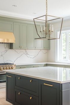 a kitchen with green cabinets and marble counter tops, an island in front of the stove