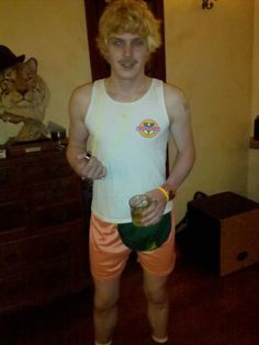 a man in orange shorts and white tank top holding a drink standing on a wooden floor