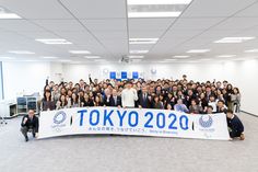 a group of people posing for a photo in front of a tokyo sign that says tokyo 2020