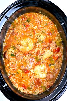 a crock pot filled with chicken and vegetable soup on top of a white table