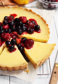 a cheesecake topped with berries and blueberries on top of a cooling rack next to a cutting board