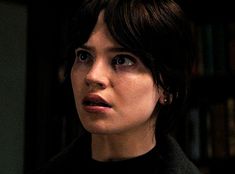 a close up of a person in a dark room with bookshelves behind her