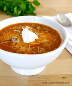 a bowl of soup with sour cream and parsley in it on a wooden table