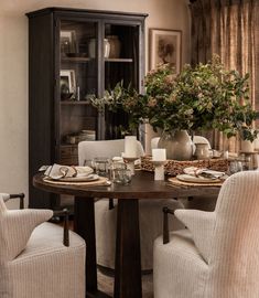 a dining room table with chairs and vases on top of it in front of a china cabinet