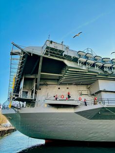 a large ship docked in the water with people standing on it's deck and some birds flying overhead