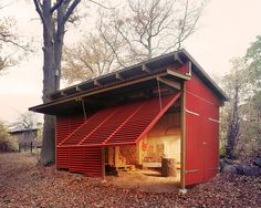 a red shed with an open door and awnings on the roof is surrounded by leaves