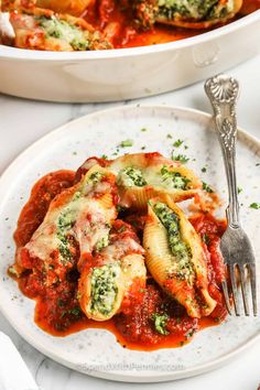 a white plate topped with pasta covered in sauce next to a casserole dish