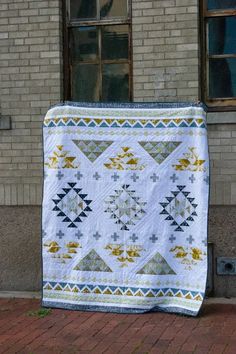 a white quilt hanging on the side of a brick building next to a window and door