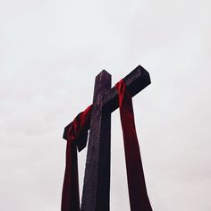 a large wooden cross with red ribbons on it's sides and the sky in the background