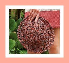 a woman's hand is holding onto a red and black straw hat in front of green leaves