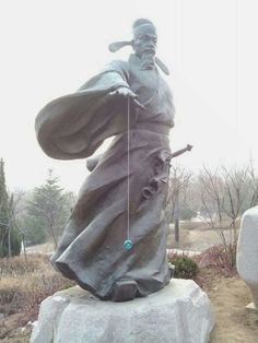 a statue of a man holding a staff in front of a white rock with trees behind it