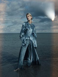 a woman standing in the water wearing a long silver coat