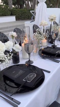 the table is set with black and white plates, silverware, candles and flowers