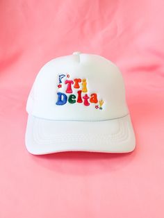 a white hat with the word delta embroidered on it sitting on a pink cloth background