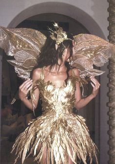 a woman in a gold dress with wings on her head and hands behind her back