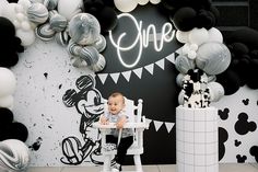 a baby sitting in a highchair at a mickey mouse birthday party with balloons