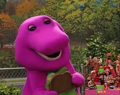 the purple dinosaur is standing in front of a group of people and holding a piece of wood