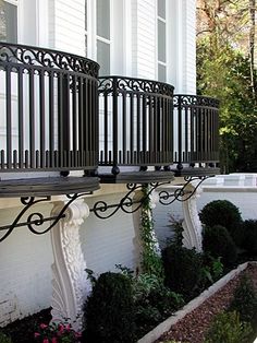 an iron balcony railing with planters and potted plants on the side of a house