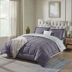 a bed with purple comforter and pillows in a room